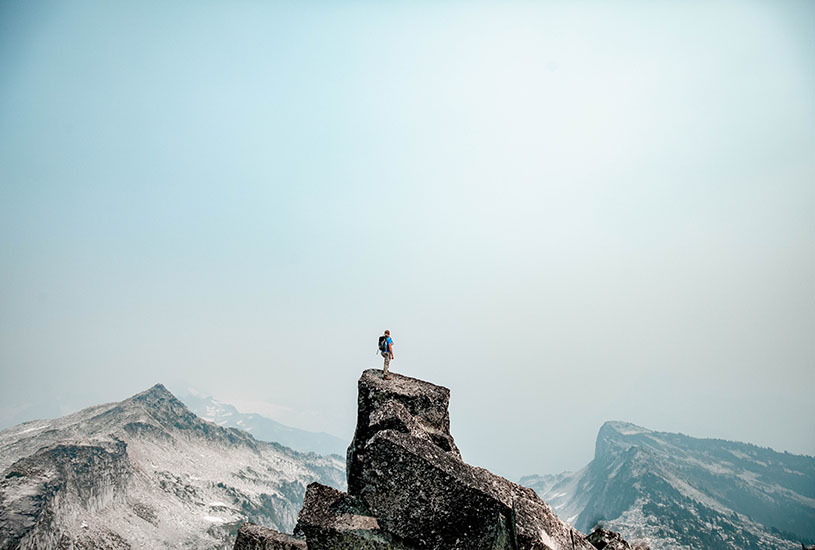 man standing on top of a mountain looking at other mountains