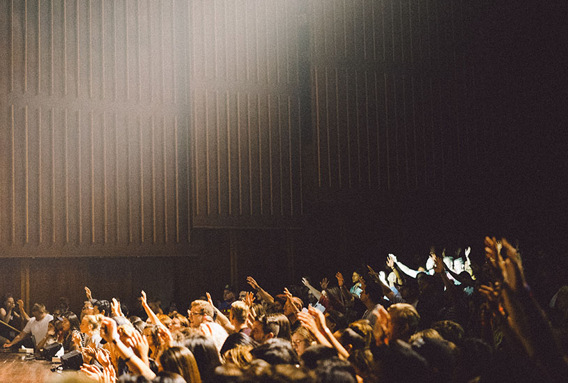 group of people in an auditorium putting their hands up in praise