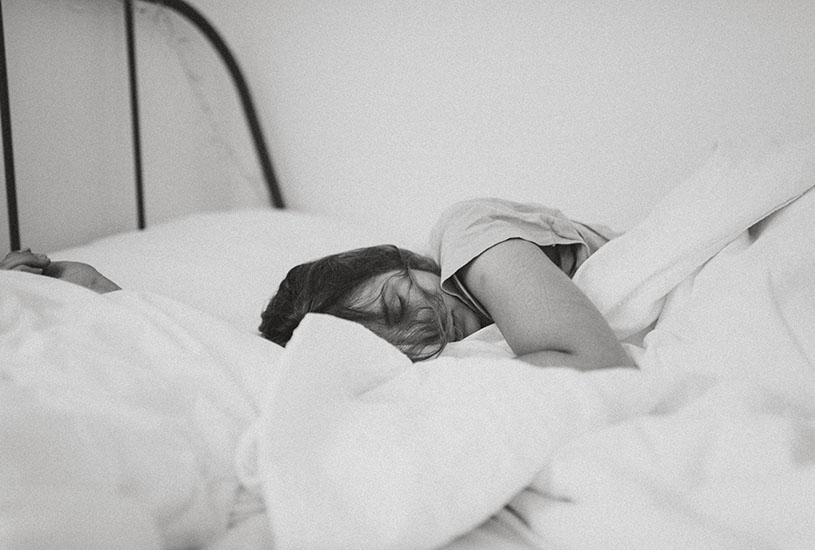 girl sleeping with white bedsheets in black and white