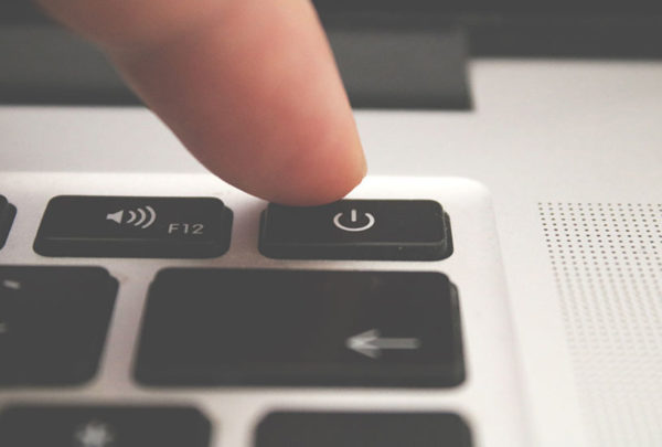 person pressing the power button on a mac
