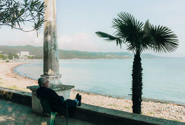 Elderly man sitting on the shade staring at the beach