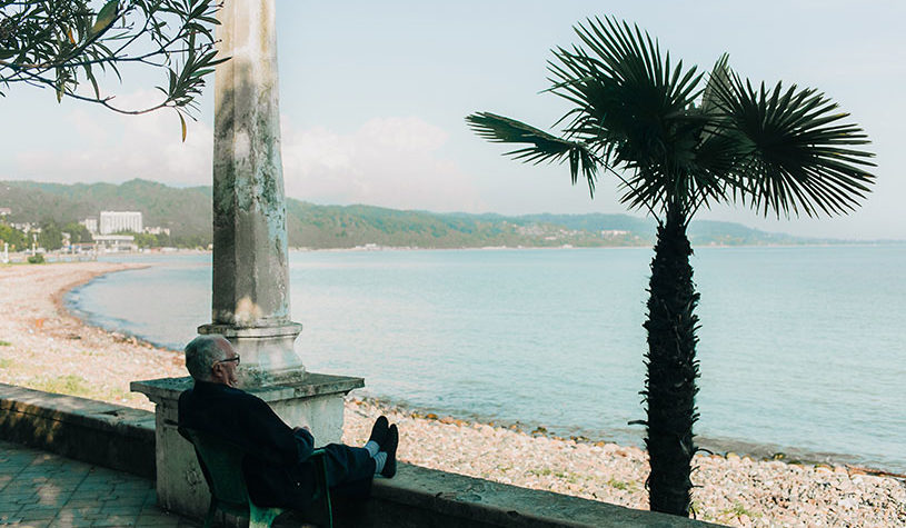 Elderly man sitting on the shade staring at the beach