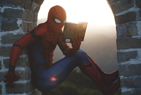 Spiderman reading a book while on a wall at sunset