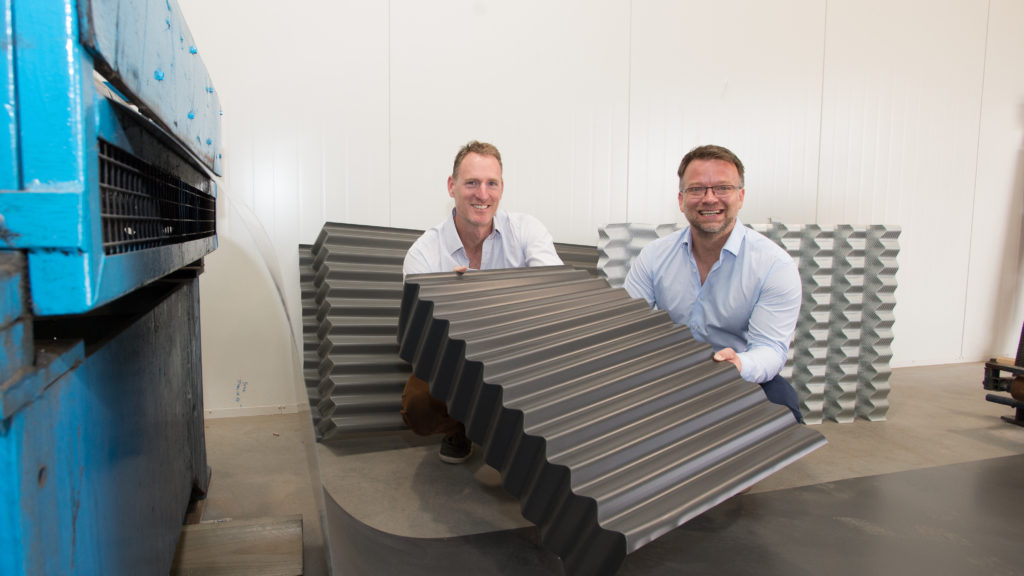 Dr Matthew Dingle and Dr Matthias Weis smiling while holding FormFlow's patented corrugated iron on factory floor.