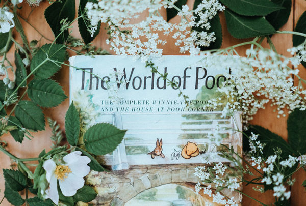 Winnie the Pooh book surrounded by flowers with green leaves.
