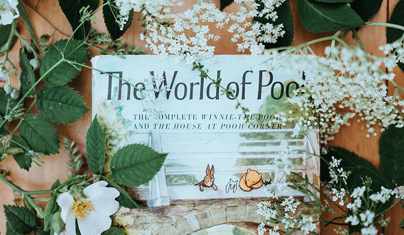 Winnie the Pooh book surrounded by flowers with green leaves.