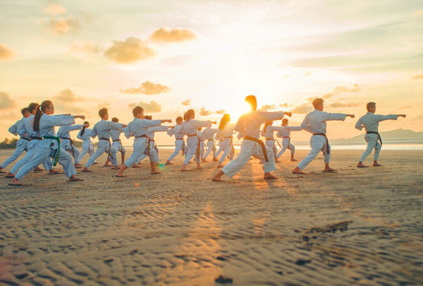 Children practicing Taekwondo on the beach at sunset