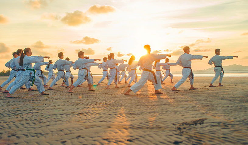 Children practicing Taekwondo on the beach at sunset