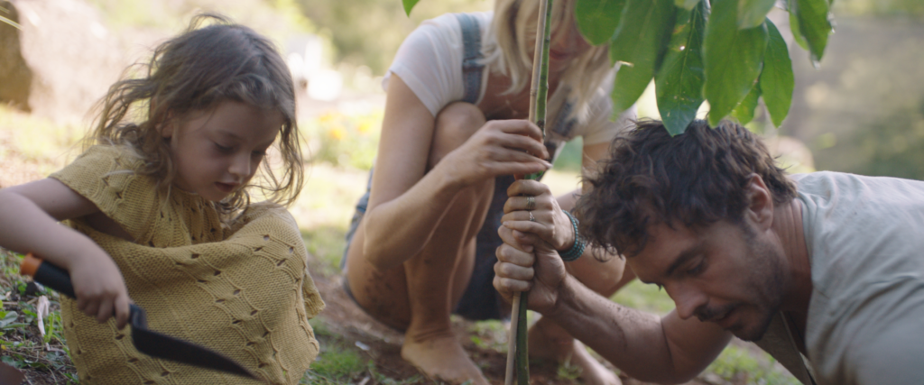 A girl holding a shovel is planting a plant with a man and a woman.