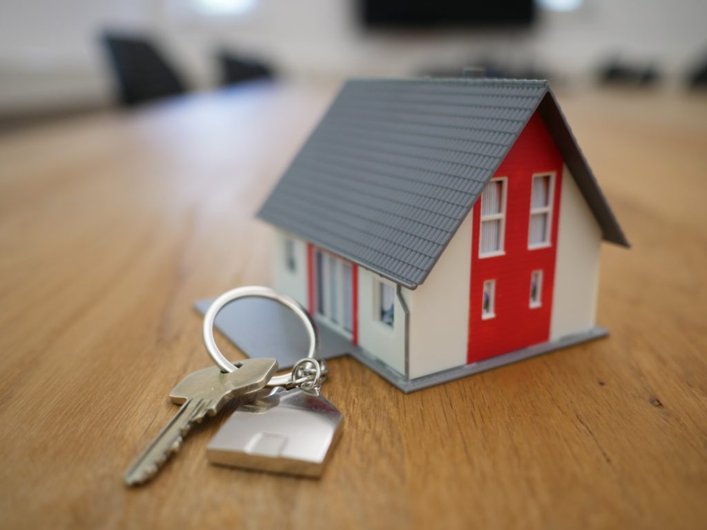 A miniature house with a keychain with keys on a hardwood table.