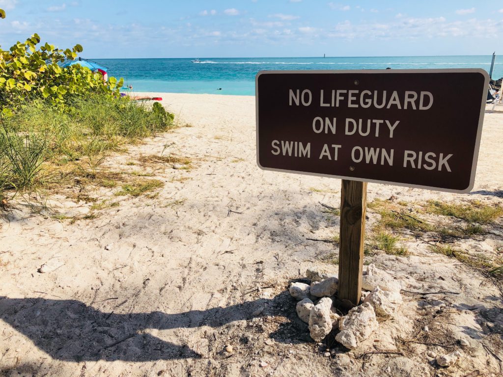 A sign at the beach entrance which says "No lifeguard on duty, swim at own risk."