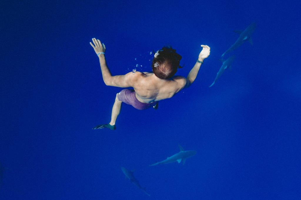 A man deep sea diving with three sharks below him.