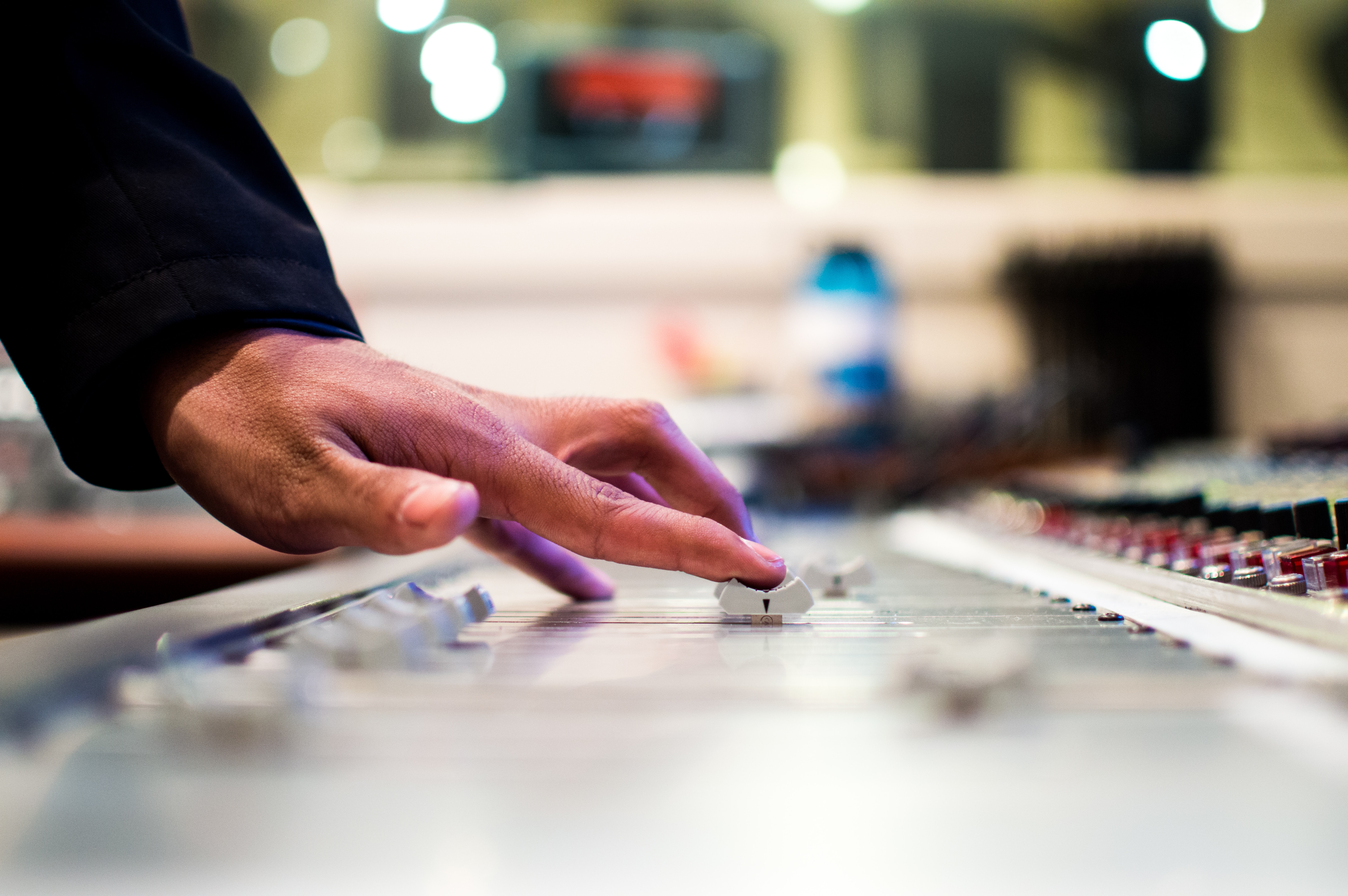 A hand adjusting dials on a mixer in a studio.