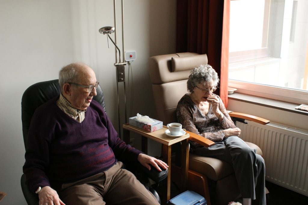 An elderly couple sitting next to each other by a window in a room.