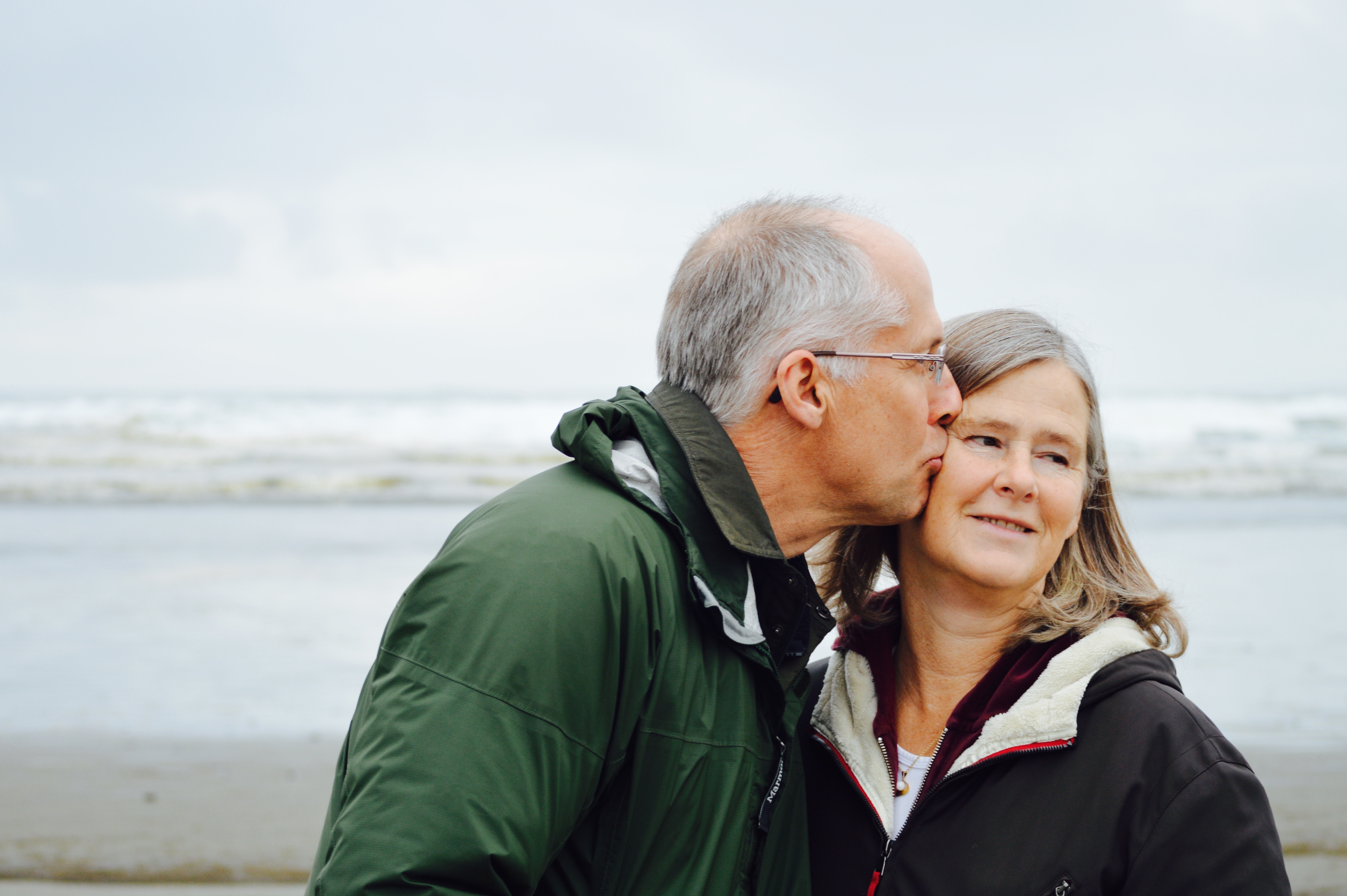 An elderly man kissing his wife on the cheek at the beach.