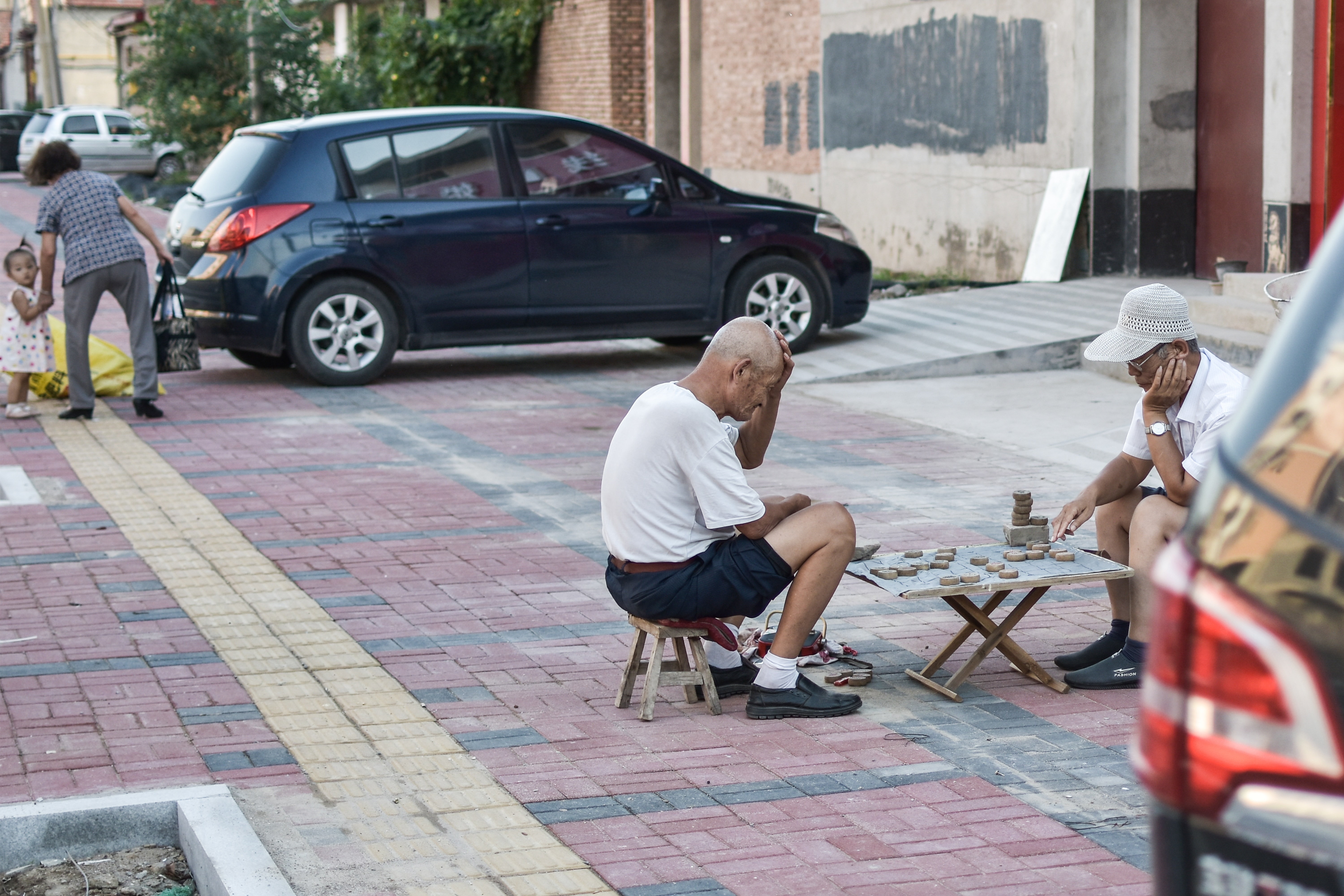 Two elderly men playing chess together on the street.
