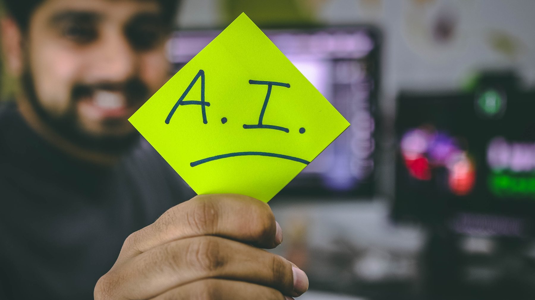 A man holding up bright, yellow sticky note with "A.I." written on it.