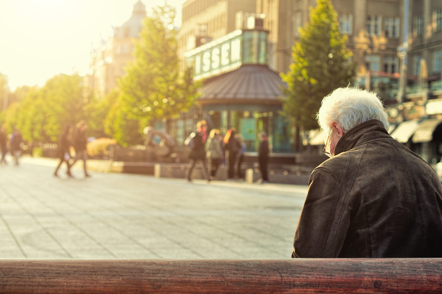 An elderly person sitting on a bench in the town centre.