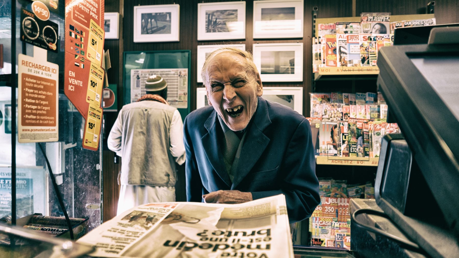 An elderly laughing and smiling at the local newsagents.