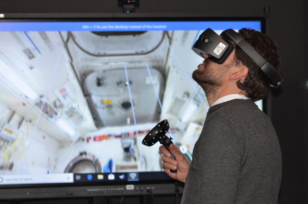 A man using a set of virtual reality goggles with a screen in the background.