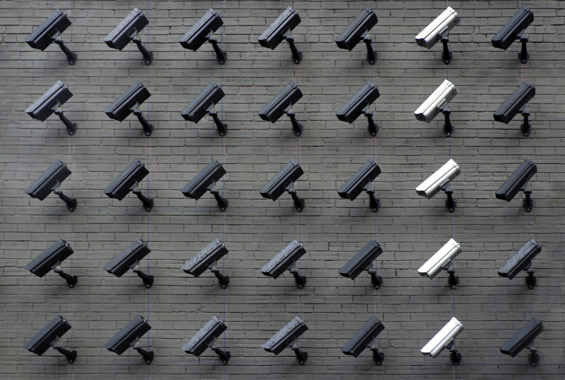 A row of security cameras on a grey, brick wall.