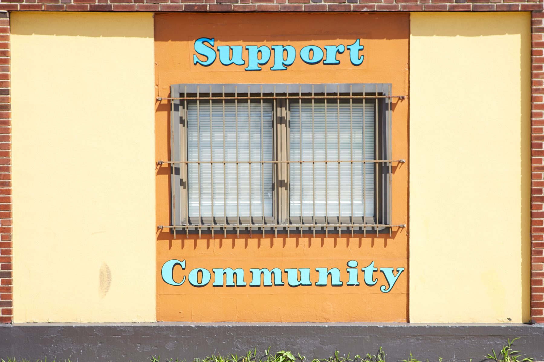 A light yellow and orange wall with a window has the words "support community" painted on it in blue.