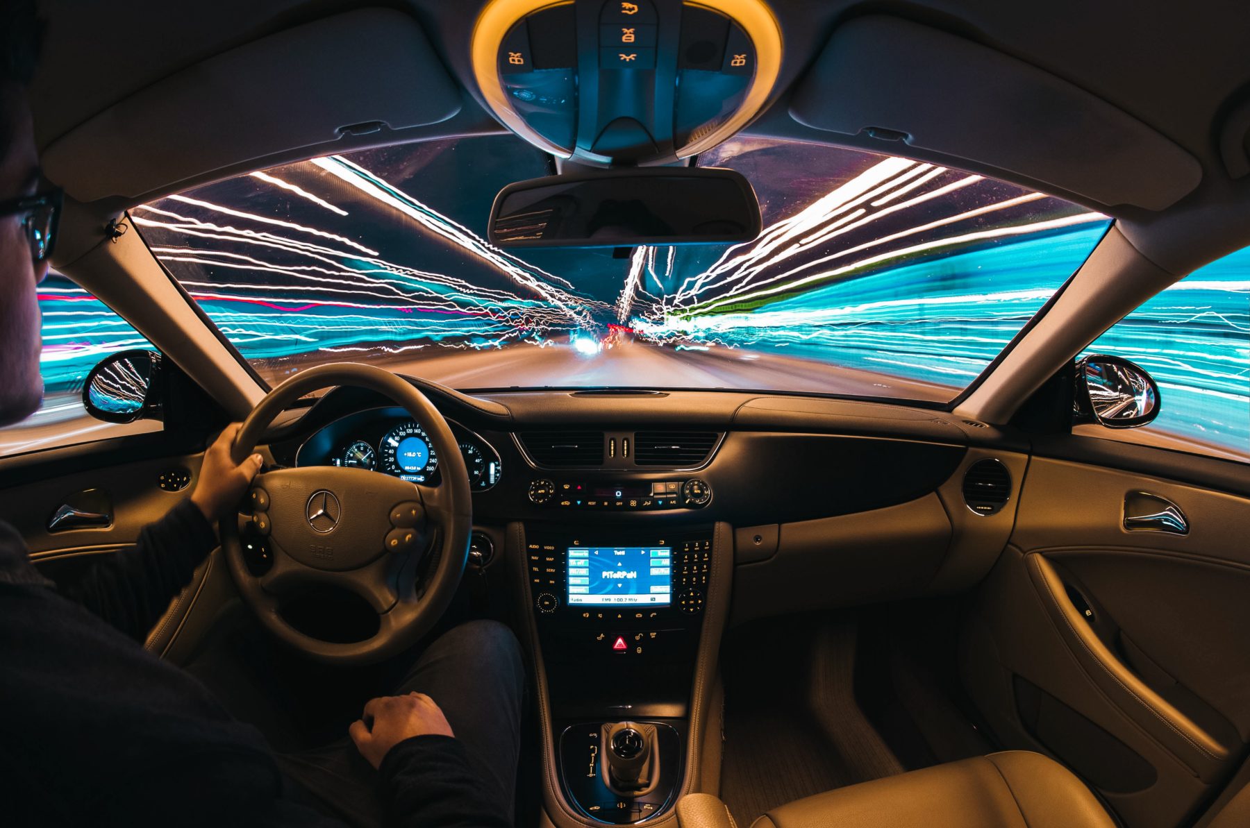 A man driving a car with long exposure lights going past in the windows.
