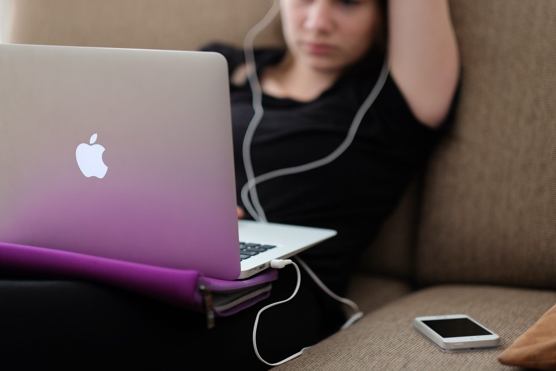 A young girl listening to music on her Apple Macbook with her iphone resting next to her.