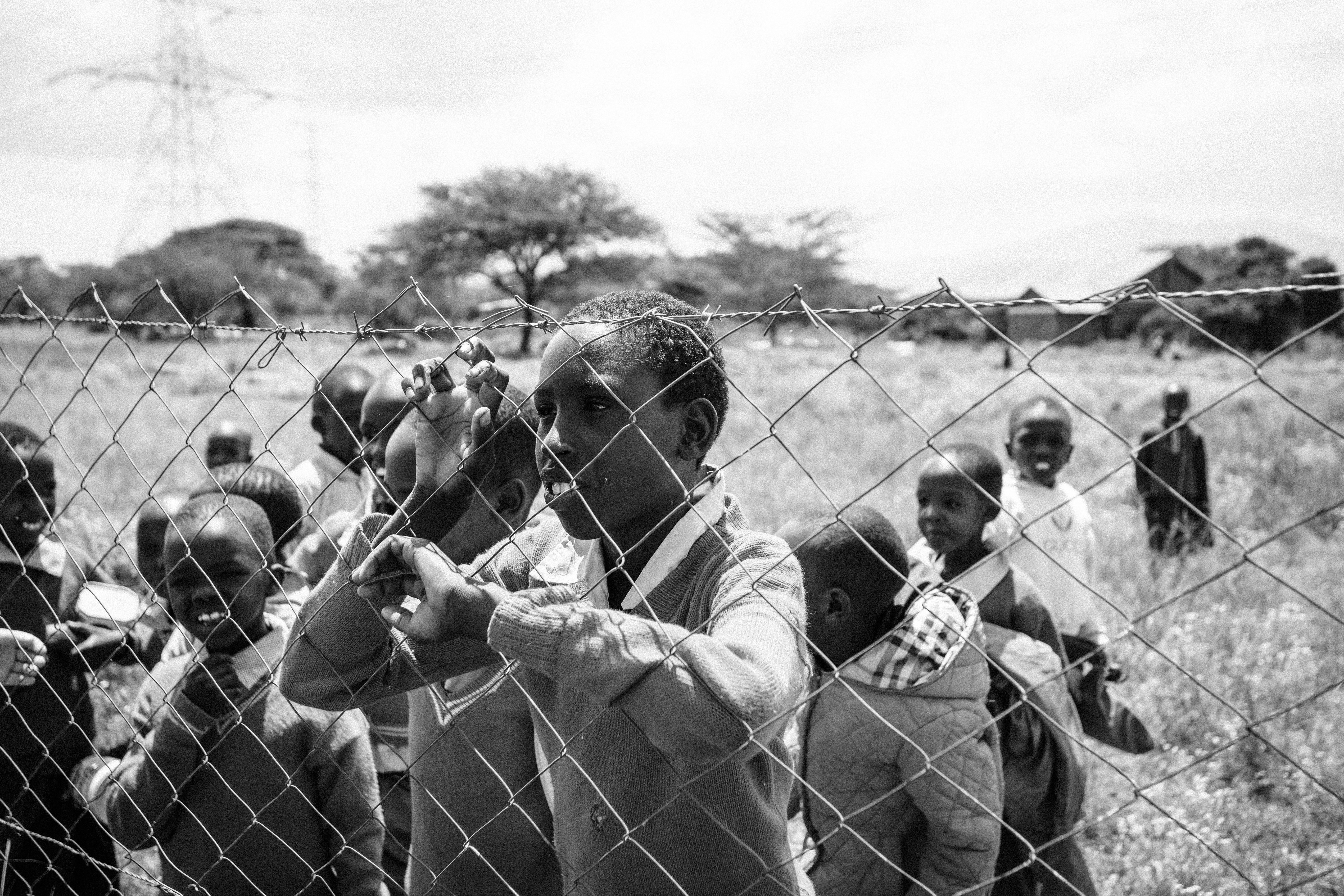 Young Kenya students resting against a metal fence.