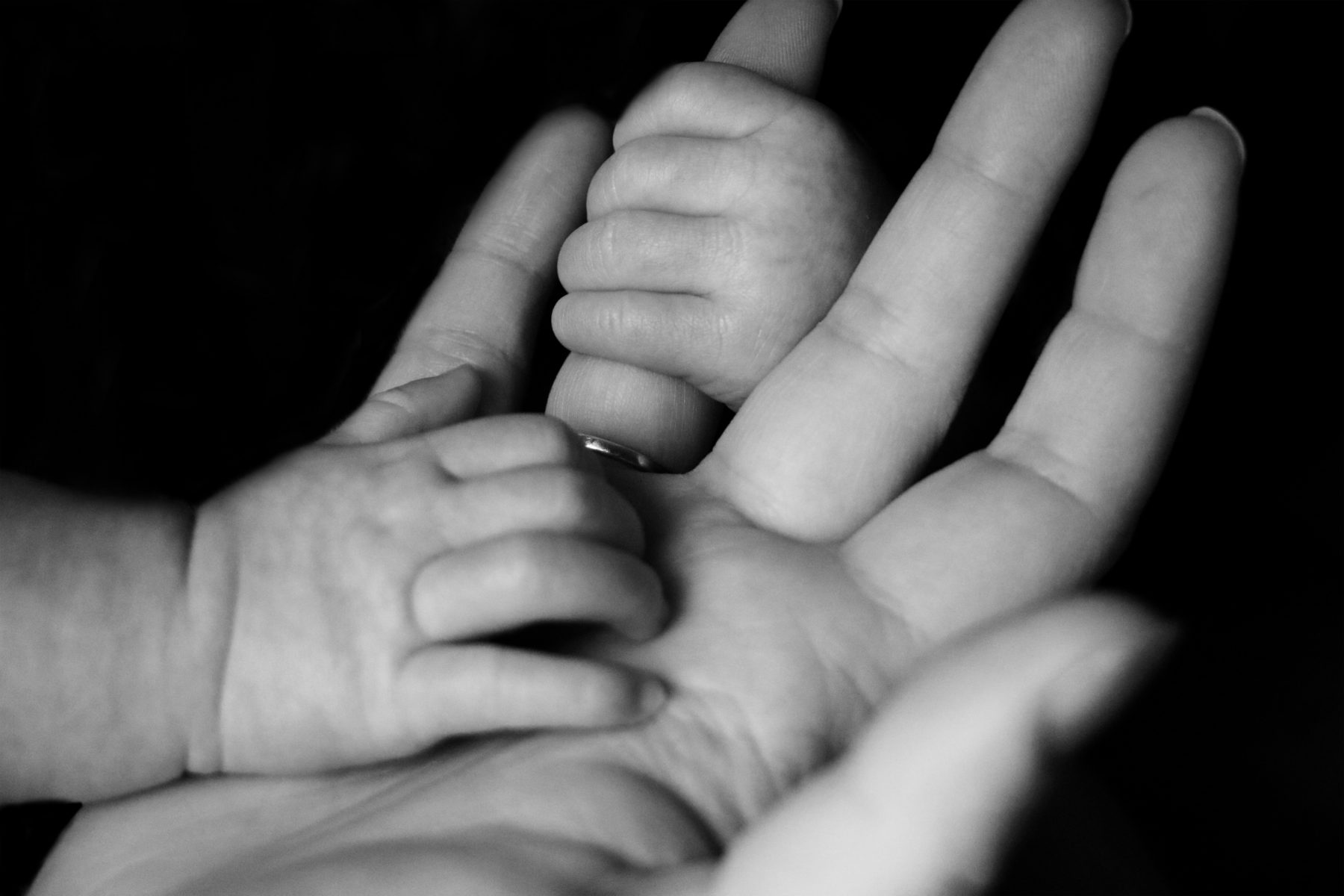 An infants hand wrapped around its mothers fingers.