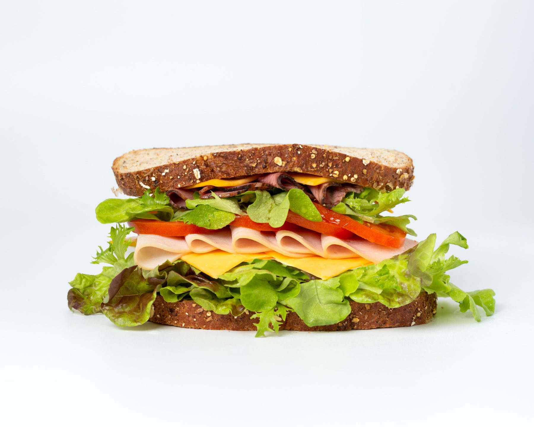 A ham, cheese, tomato and lettuce sandwich against a white background.