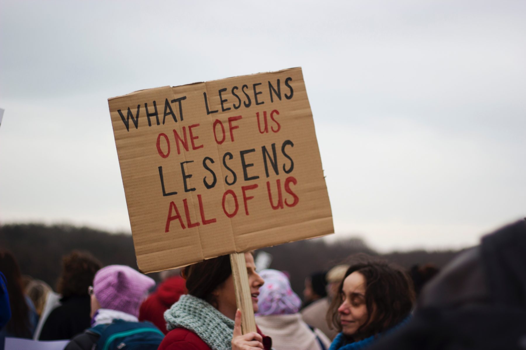 A young woman holding up a placard which says "what lessens one of us lessens all of us."