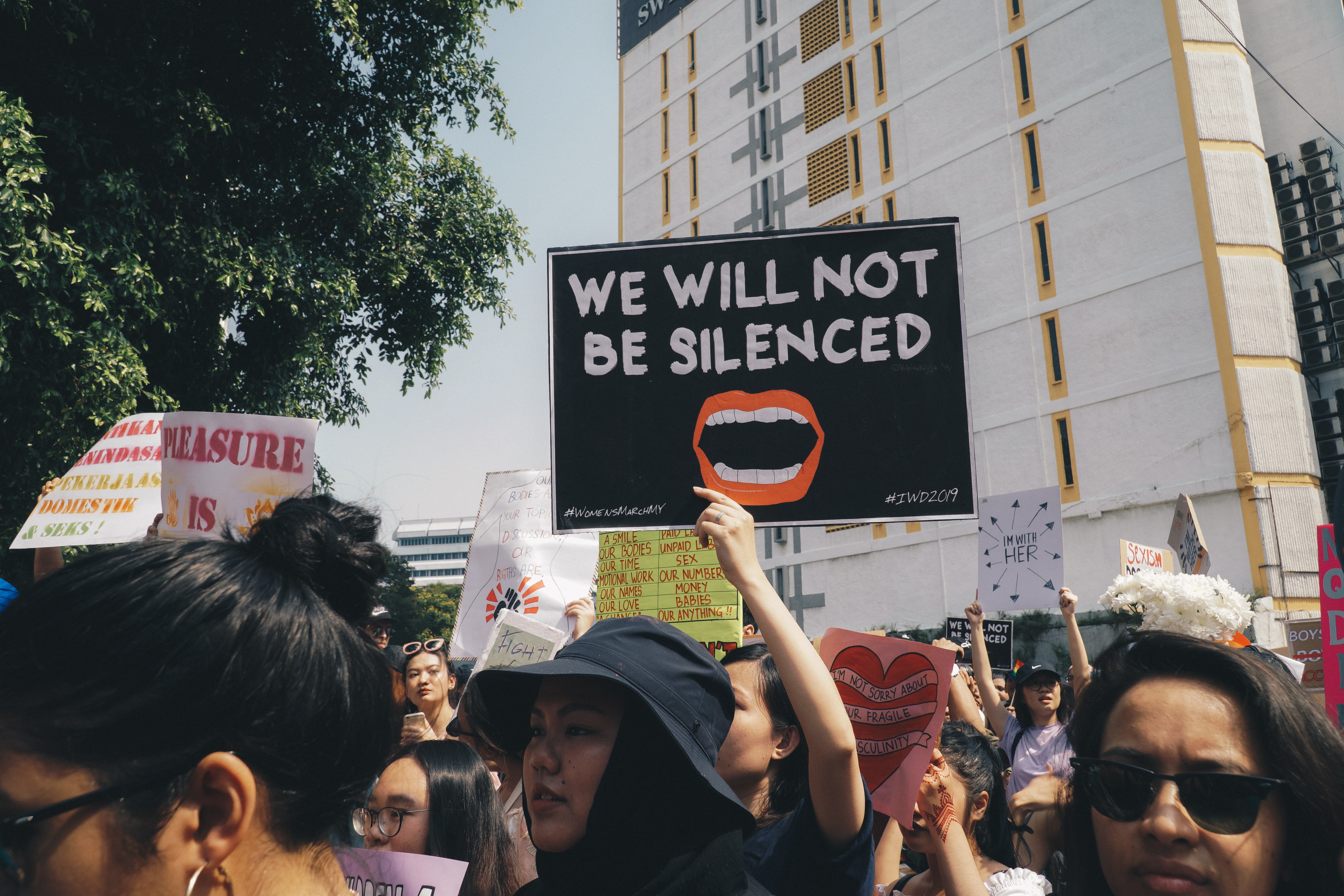 A young woman in a protest holding a placard that says "we will not be silenced."