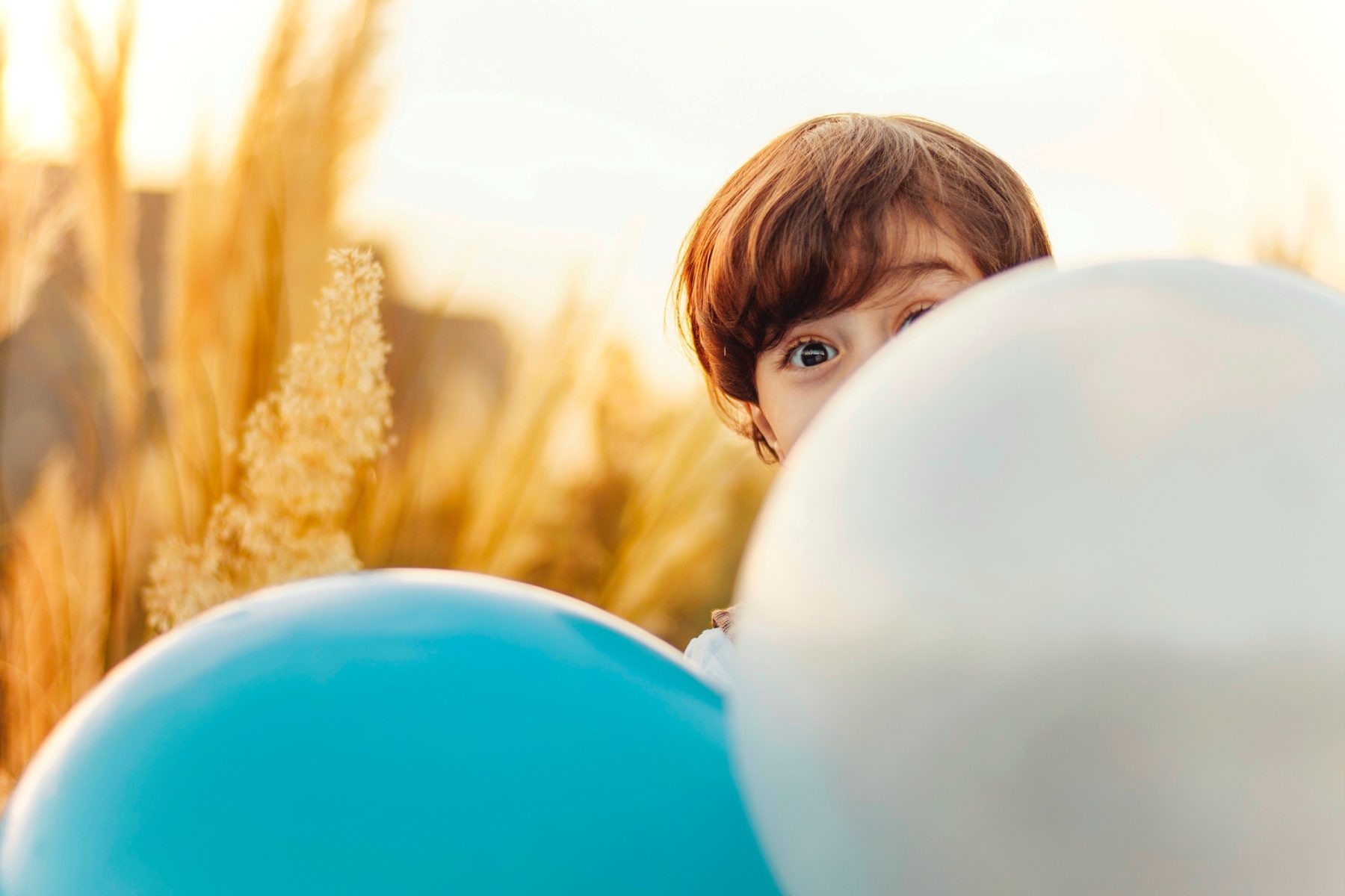 A young boy hiding behind a blue and silver balloon.