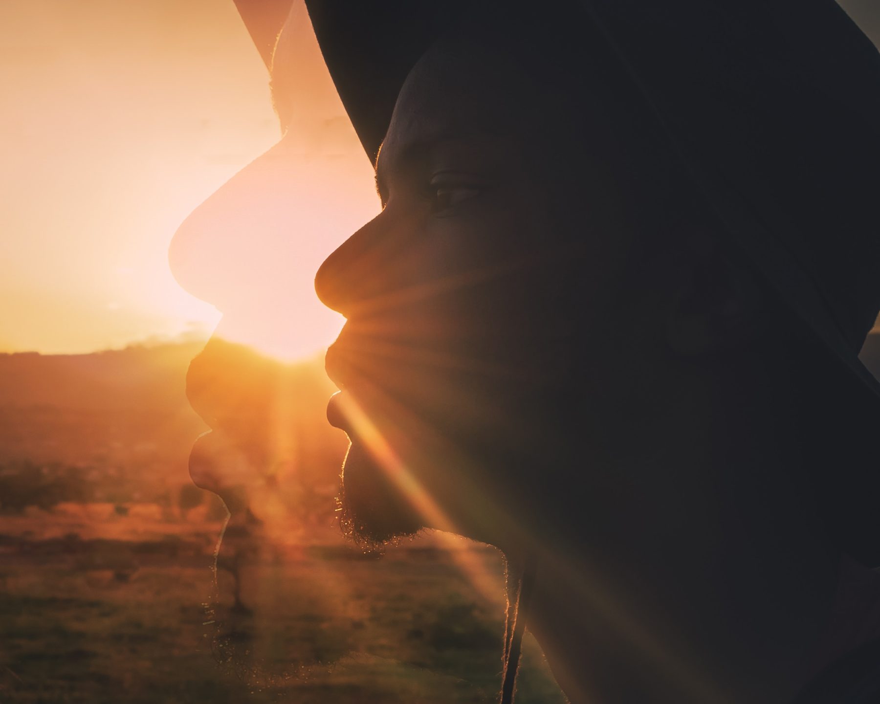 A portrait of a young, Kenyan man wearing a hat with the sun setting in the background.