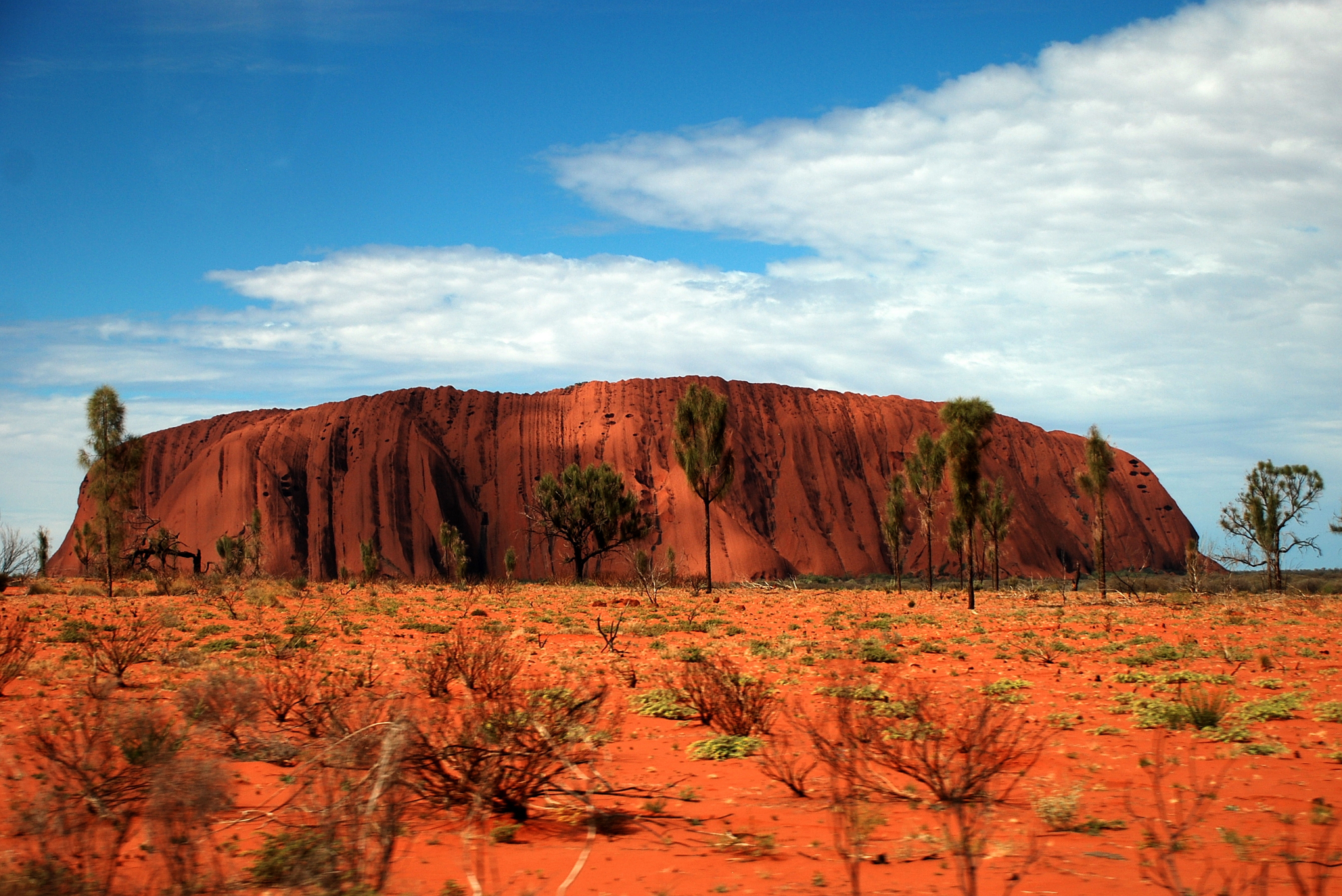 An image of Uluru with the dusty desert sand in the foreground.