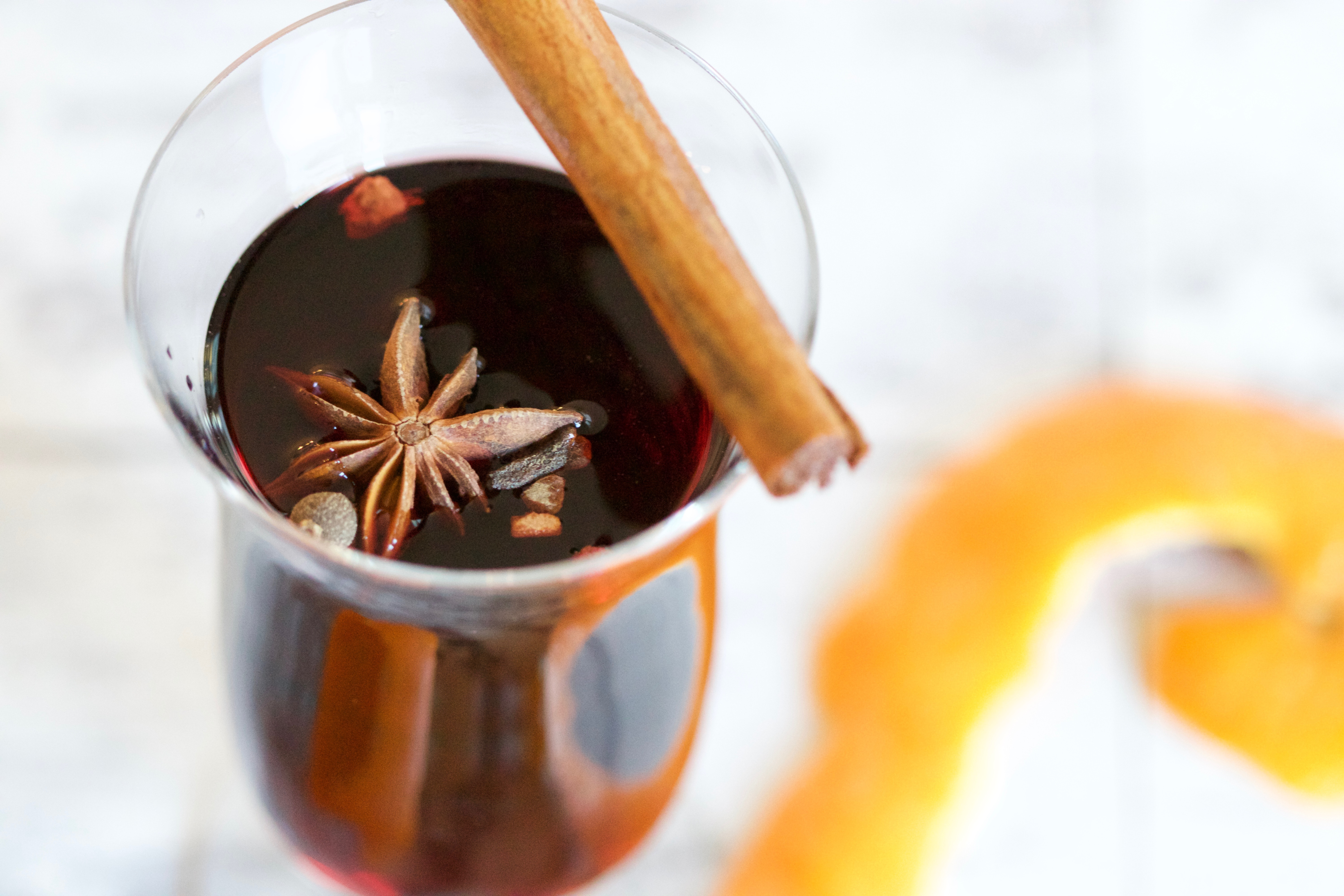A glass of mulled wine with a stick of Cinnamon balanced on the rim.