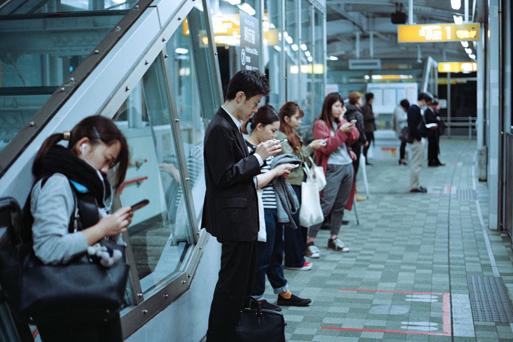 A group of people waiting for a train in Japan, all on their phones.