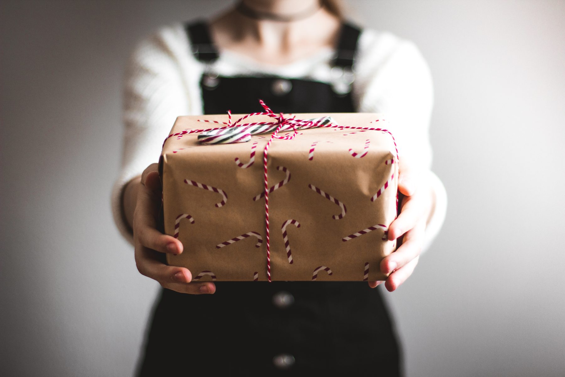 A person holding a wrapped Christmas present, with arms outstretched.