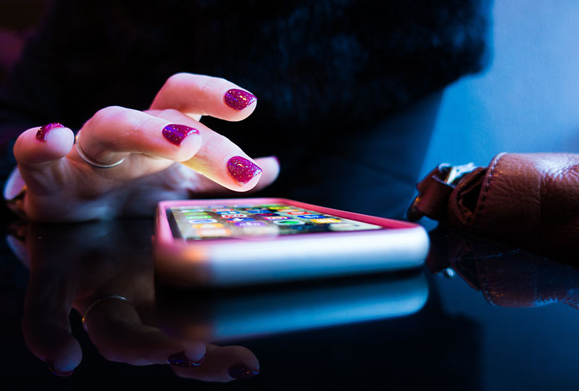 A hand scrolling through a smartphone on a black table.