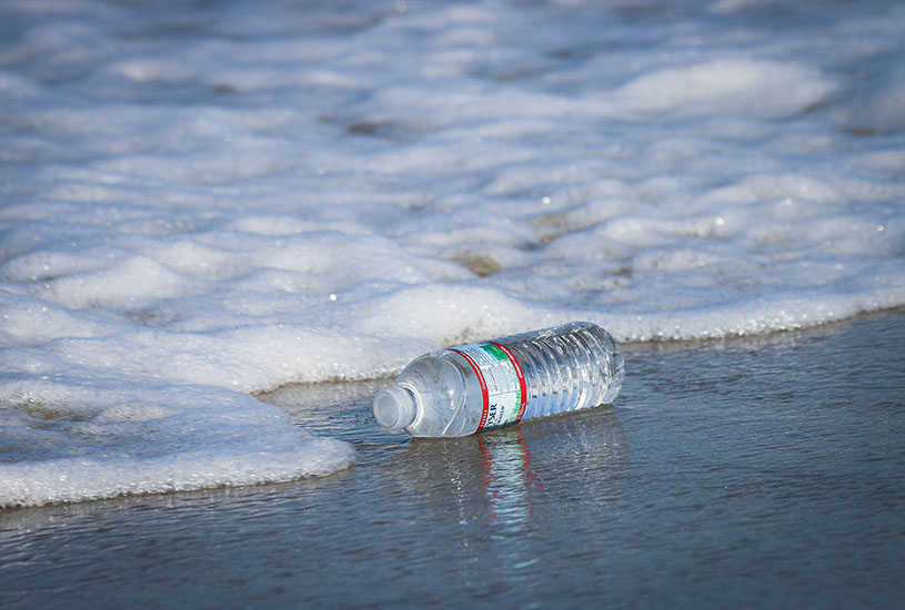 A discarded plastic water bottle floating in the waves at the beach.