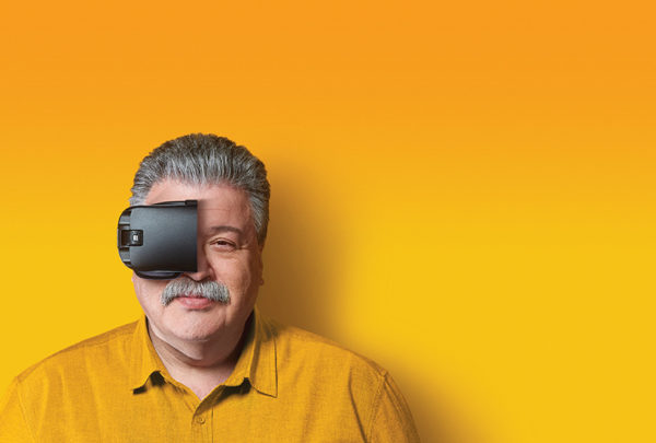 Kon Mouzakis against a yellow background with half a VR headset on his face.