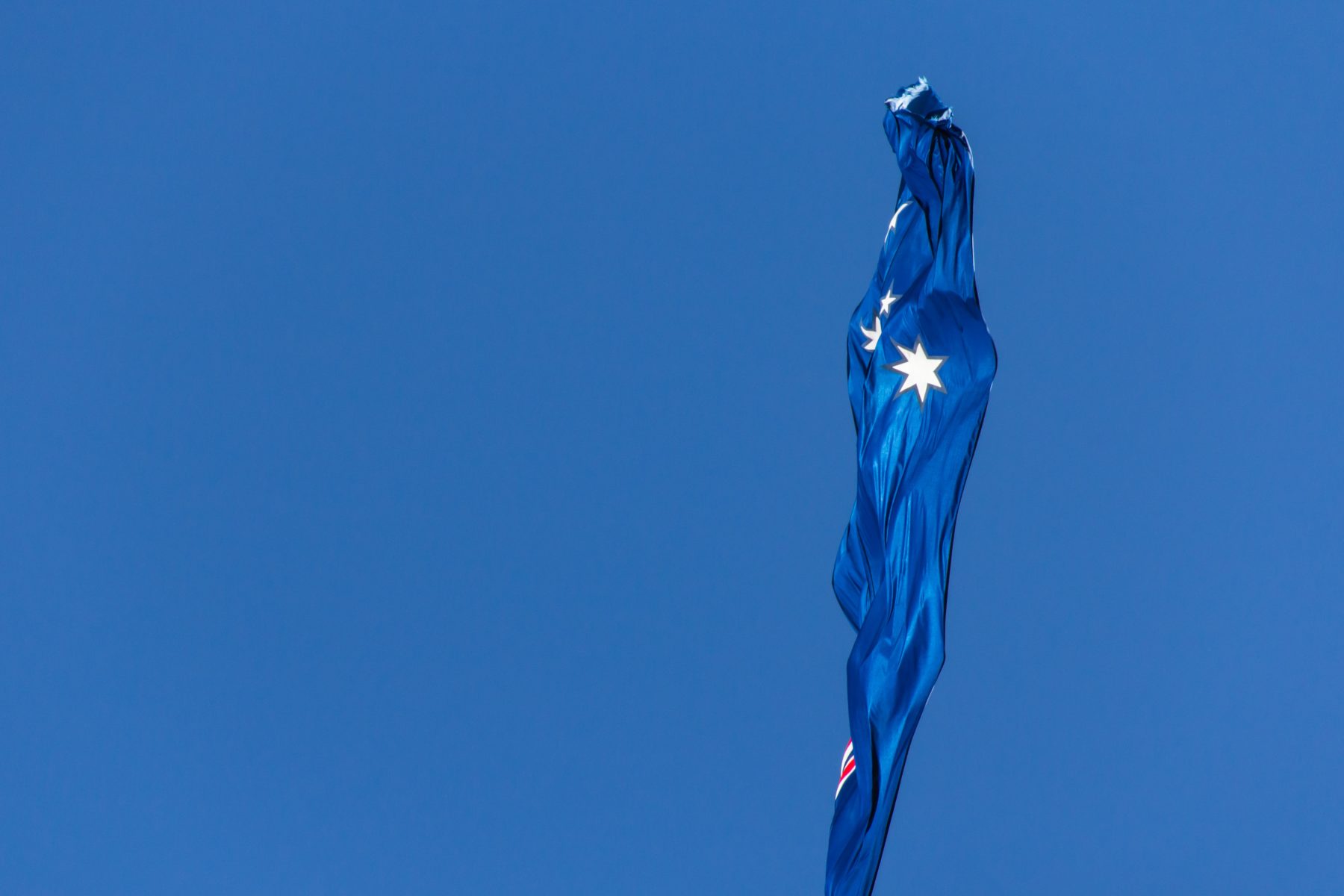 The Australian flag blowing in the breeze with blue sky in the background.