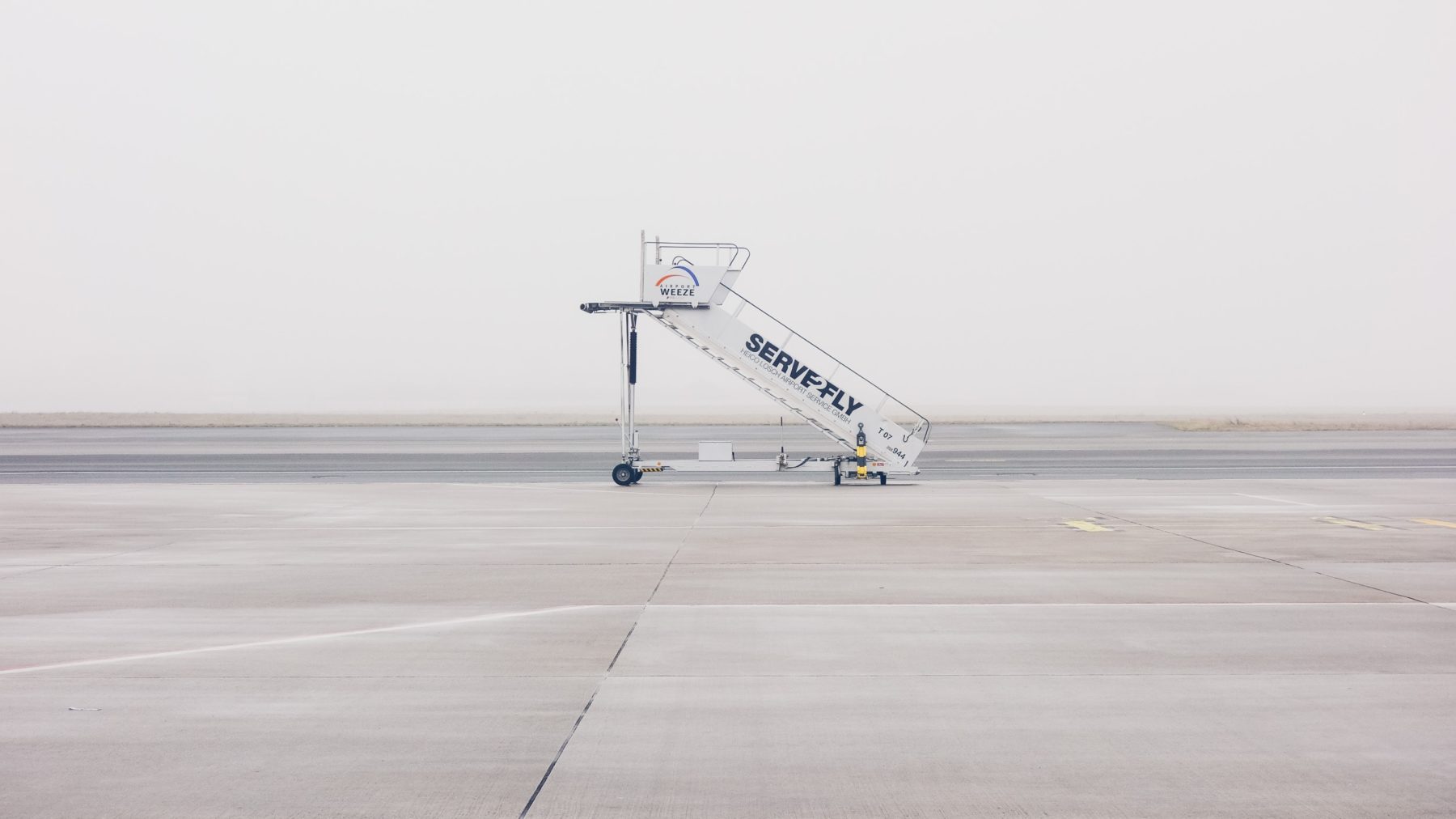 A deserted airport runway with a lone set of aircraft stairs on it.