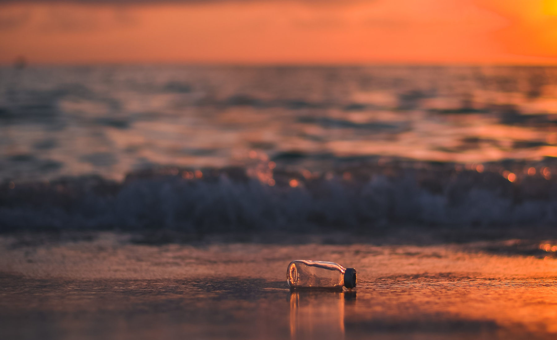 A lone water bottle on the beach with the sun setting in the background.