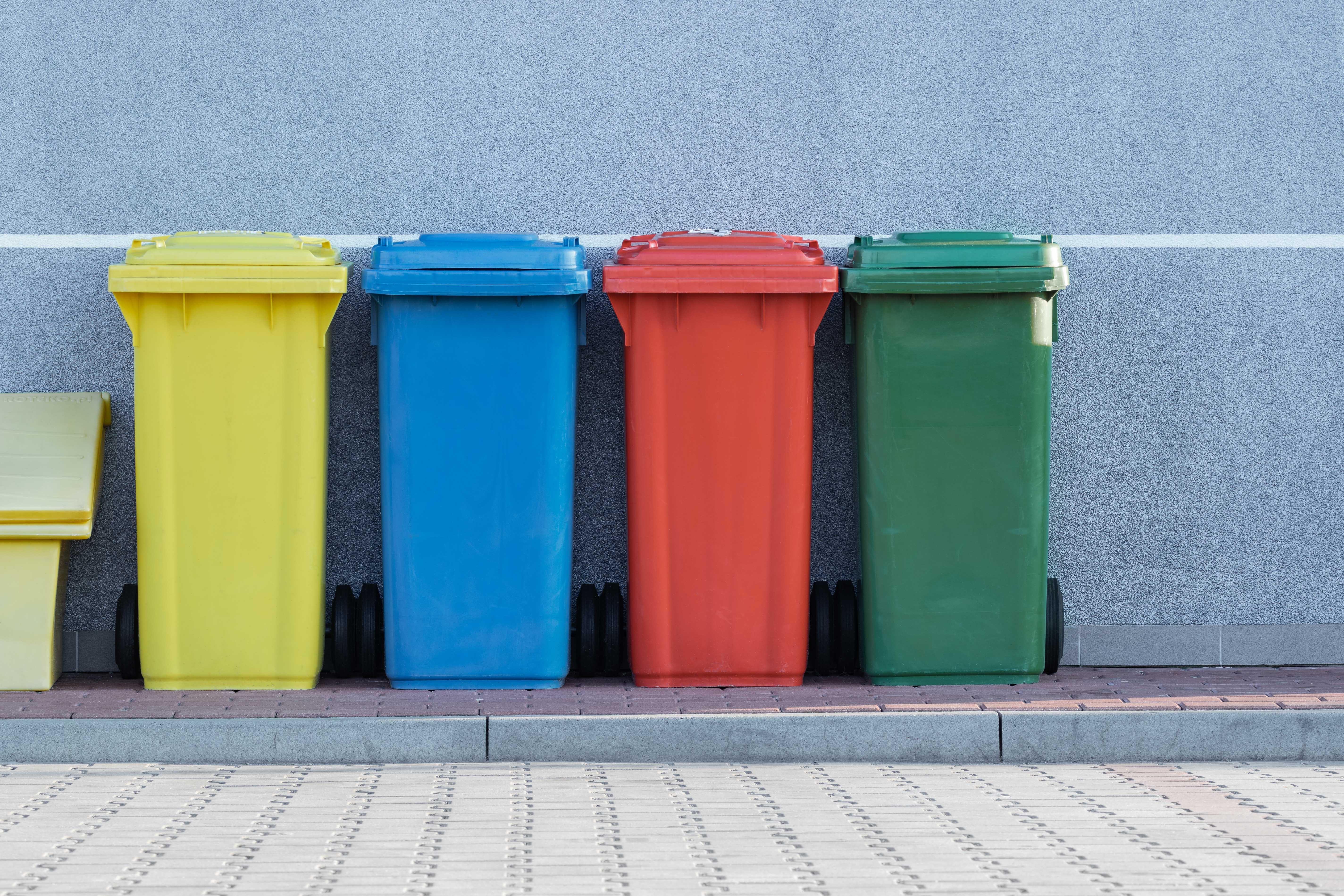 A yellow, blue, red and green bin in a line on the side of the road.