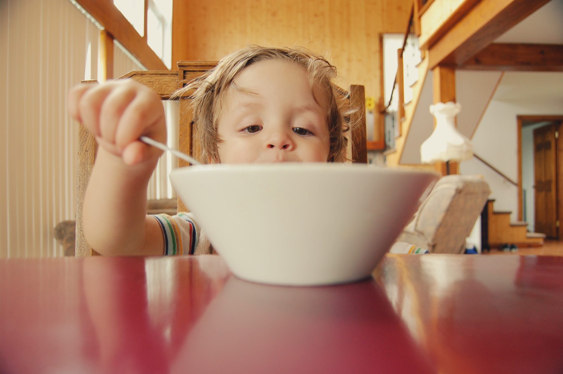 A young boy eating out of a bowl with a spoon at the dining table.
