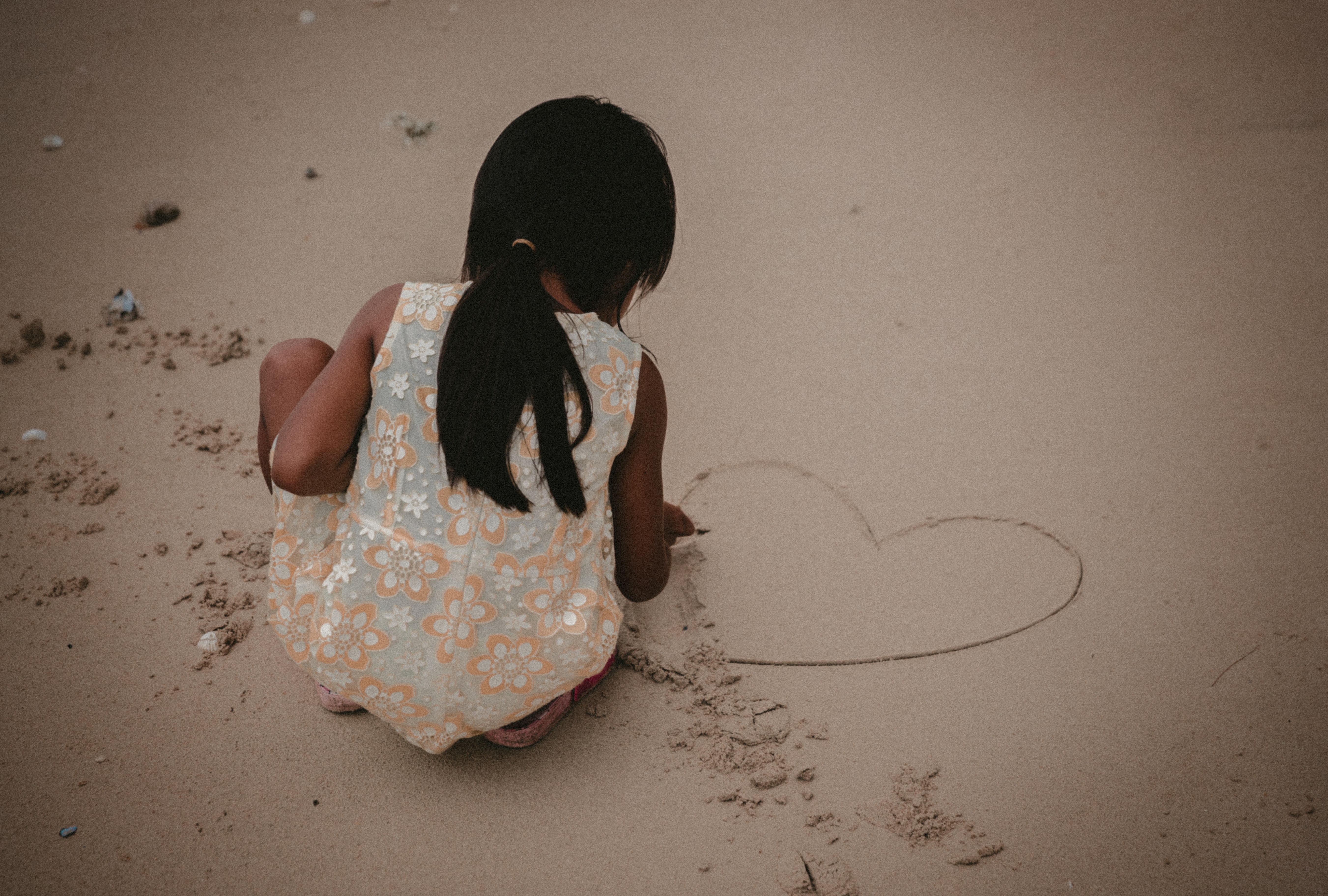 A young, Islander girl drawing a love heart in the sand on a beach.