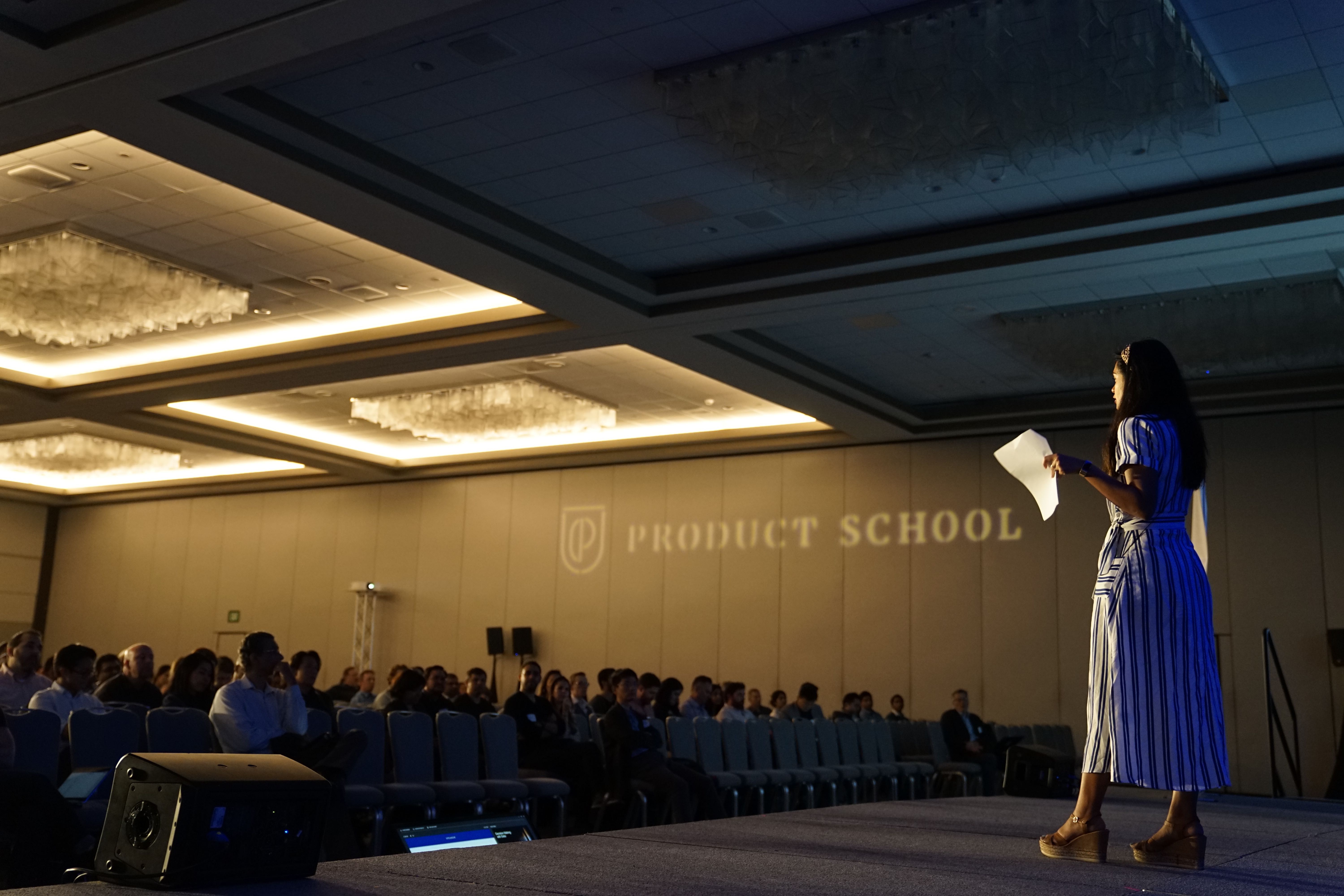 A young woman presenting to an audience on a stage at Product School.