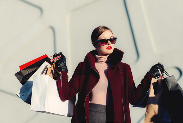 A young woman wearing sunglasses holding shopping bags in both hands.